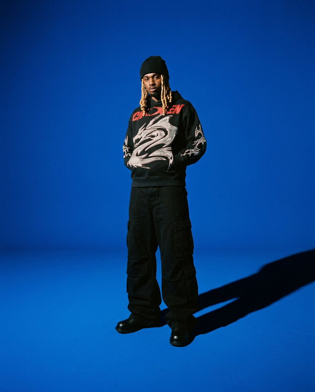 Man in a black Chosen dragon hoodie standing in an all-blue studio