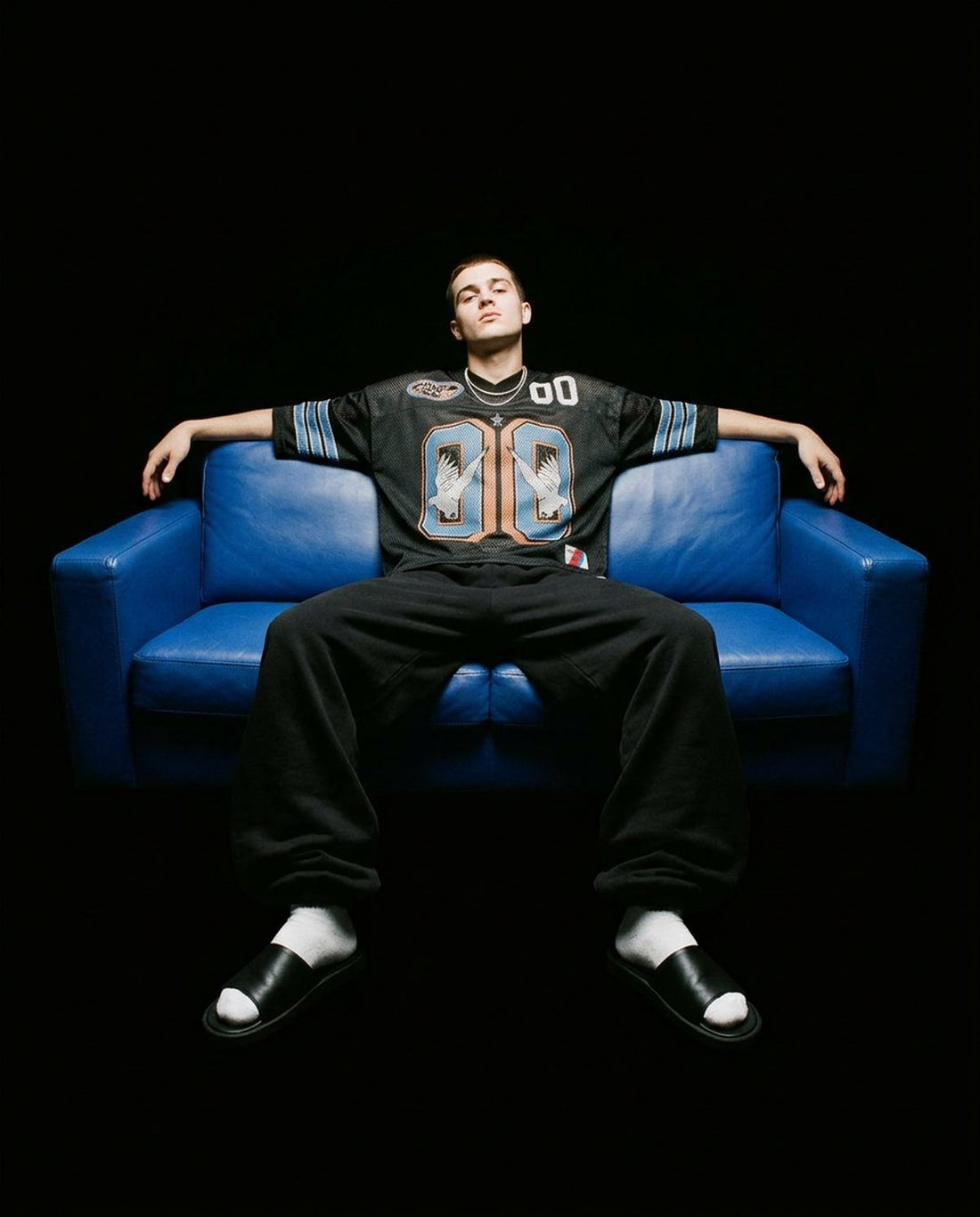 Man in a Genuine Doves jersey sitting on a blue leather sofa in the dark