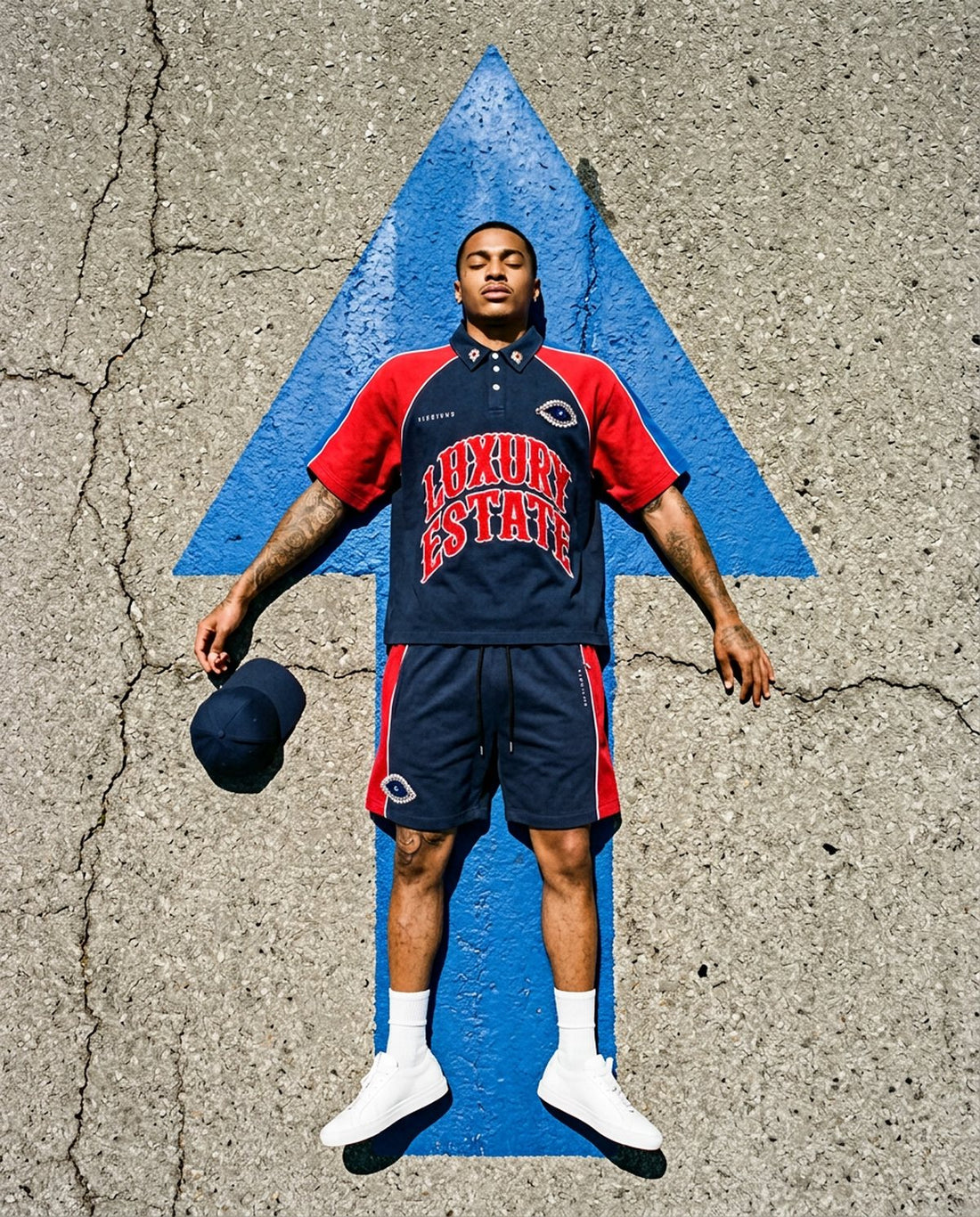 Man in a Vie+Riche Luxury Estate short set lying on a blue arrow painted on asphalt